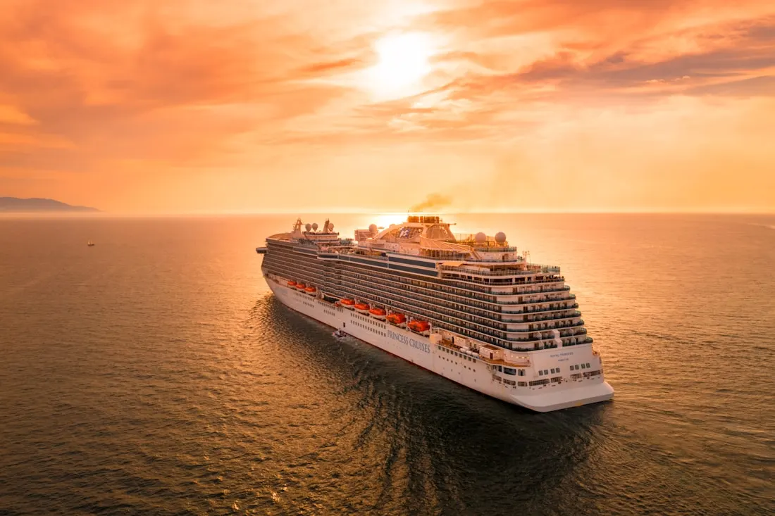 Cruise ship at sea under an orange sunset, seen from above