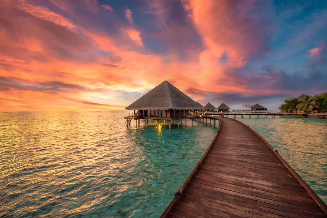 Boardwalk leading to overwater bungalows at sunset