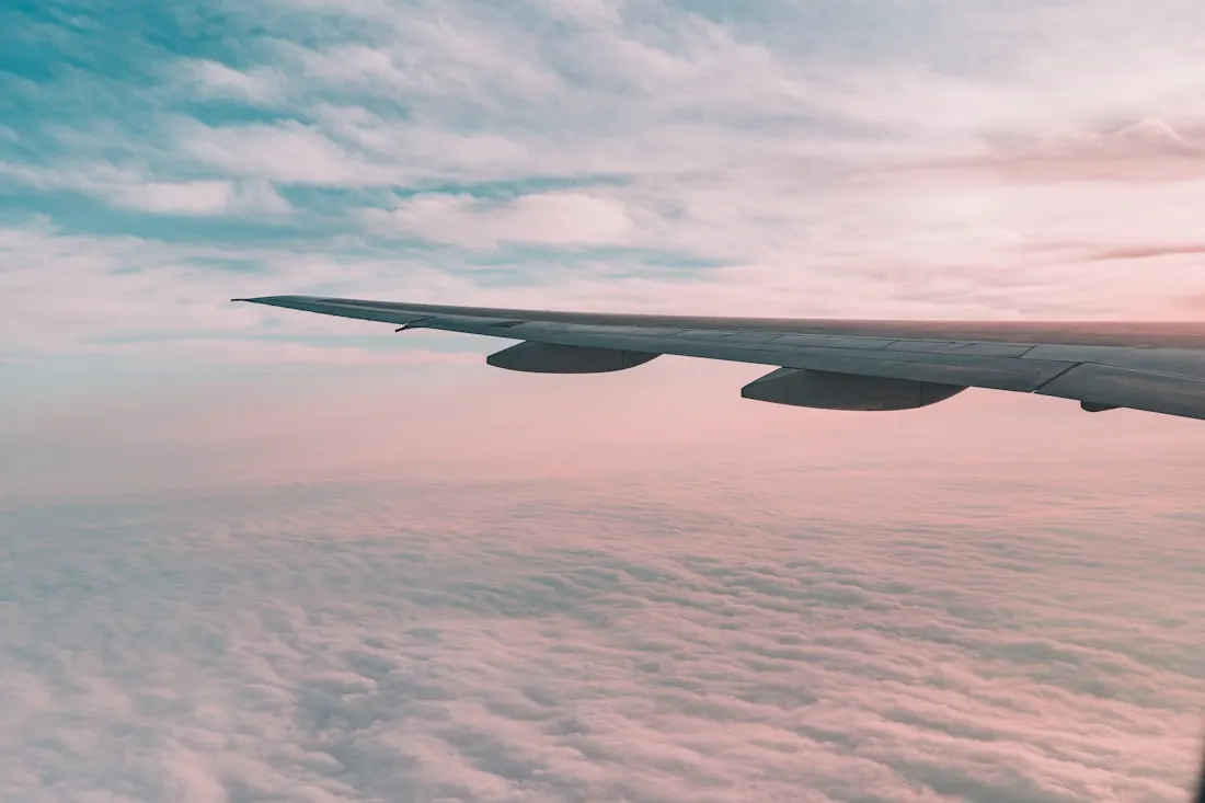 Airplane wing over soft pink clouds at cruising altitude